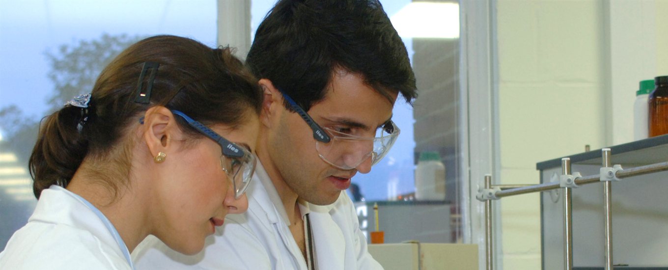 2 students in white labcoats and blue goggles working together