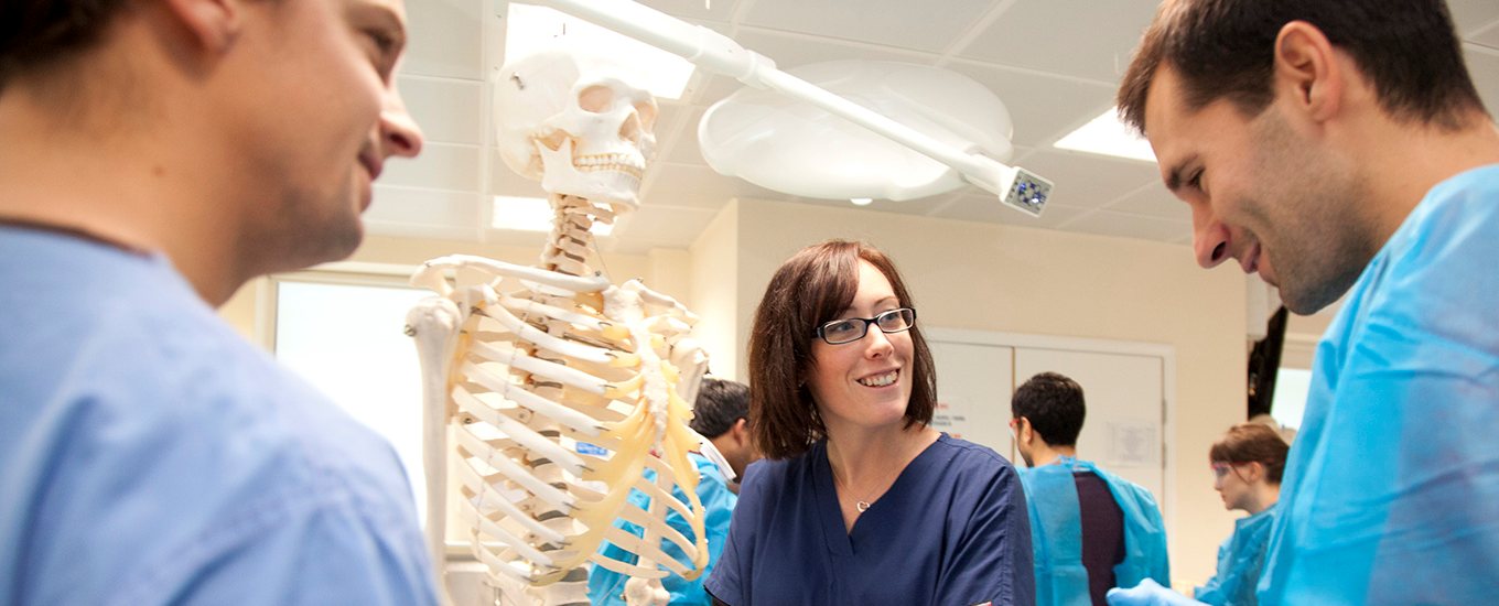Staff and students standing with a skeleton in an anatomy lab