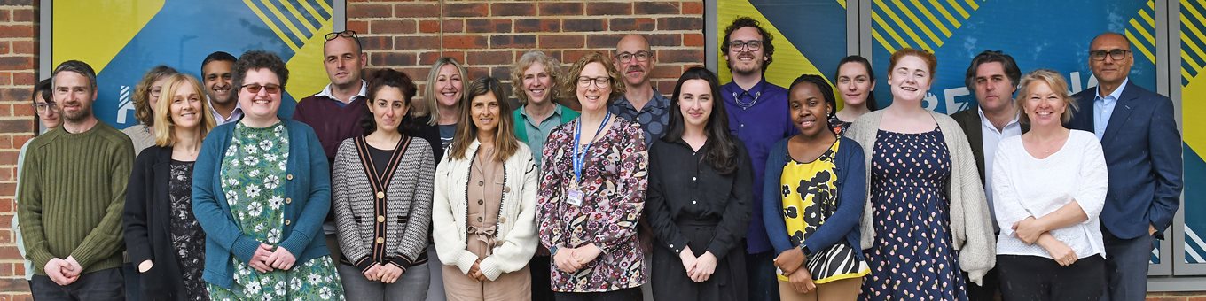 A group photo of the primary care team at BSMS. The team are stood in front of a wall with bright artwork on it