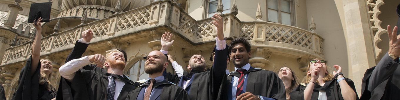 Graduates in gowns throwing mortar boards in the air outside Brighton Pavilion