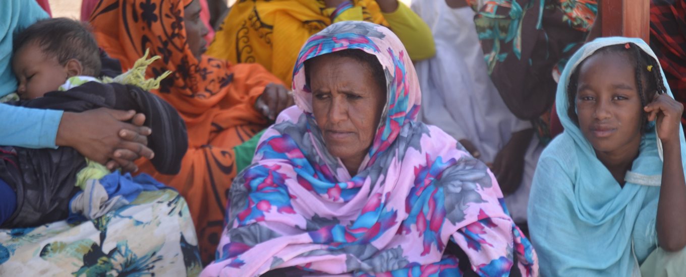 Woman in a colourful headscarf sitting next to a sleeping child being hugged by their mother