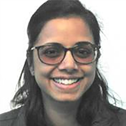 A head and shoulders shot of Dr Menaka Jegatheesan smiling and wearing glasses in front of a white wall