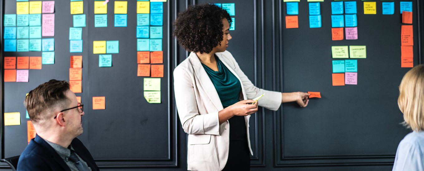 a woman pointing at post it notes on a board while other people look