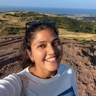 A selfie photo of Isra Husain outside in front of a scenic background