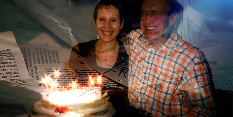 A father and daughter standing together smiling behind a birthday cake with sparklers