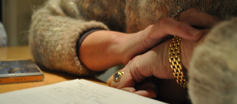 folded hands on a table, wearing a gold ring and bracelet, looking over a notepad