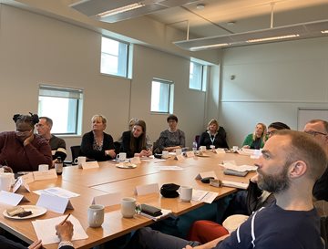 A group of people around a table having a discussion and listening to a speaker