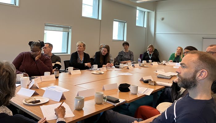 A group of people around a table having a discussion and listening to a speaker