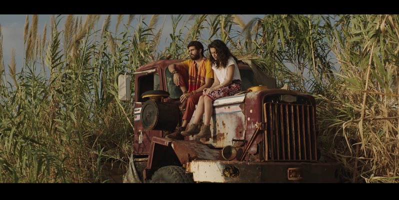 A screenshot from the film Farah showing two people sat on a rusty car