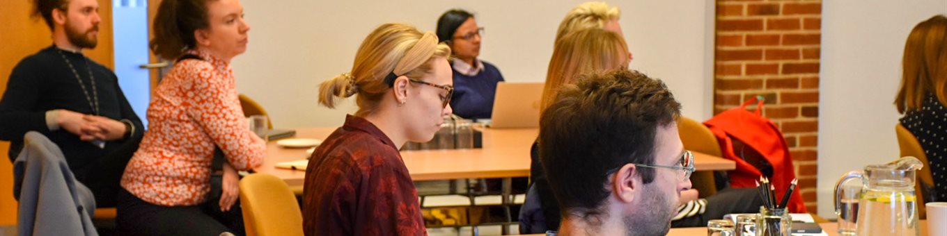 A group of researchers sat around tables listening to a talk in a conference setting