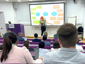 Dr Liz Ford from BSMS presenting in front of a screen to people in a lecture theatre