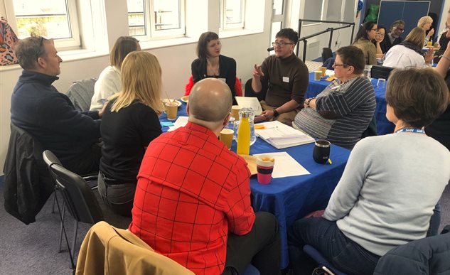 Groups of people in a room sitting round tables talking