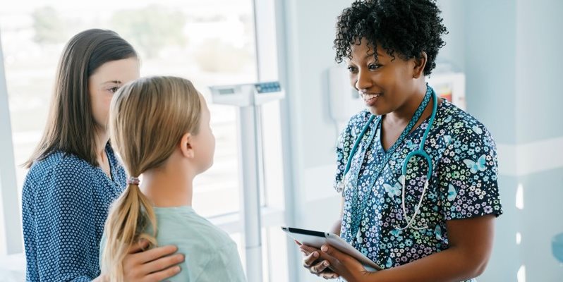 A nurse in scrubs talking to a parent and child