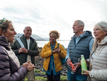 A group of people stood talking outside in the countryside next to the water