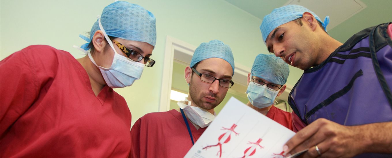 Surgeon talks to 3 students in red lab coats while they look at training materials together
