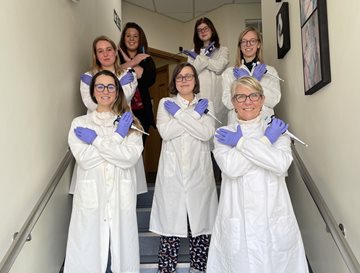 Women in lab coats making an X with their arms