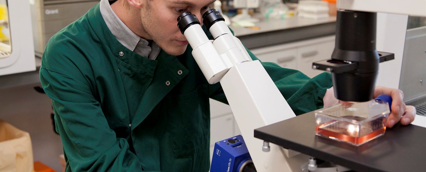 Student in a green lab coat looking down a microscope