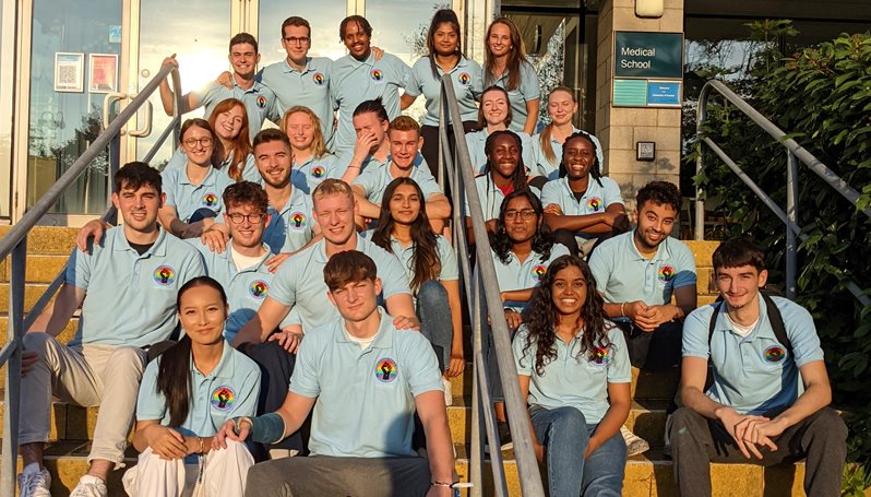 A group of medical students sat on steps outside in matching polo shirts