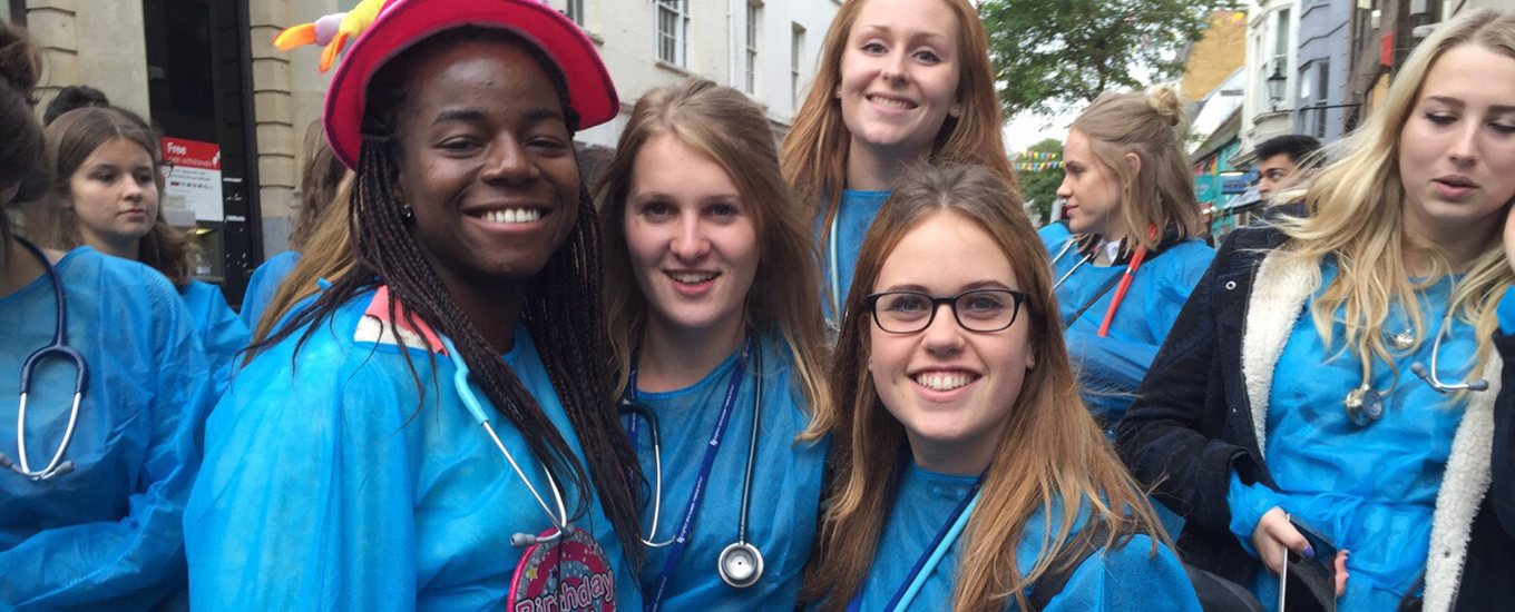 Group of smiling MedSoc members wearing gowns and stethoscopes on fundraising event