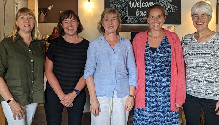 Five woman stood in a line next to each other smiling at the camera in a pub or restaurant setting