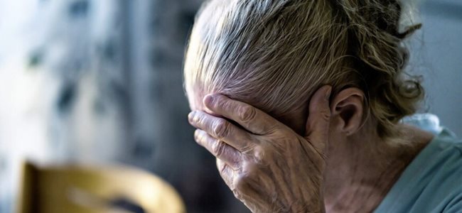 An elderly woman holding her head in her hands