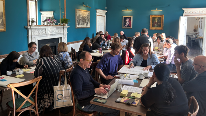 A group of people sitting around a table in conversation in a room with blue walls