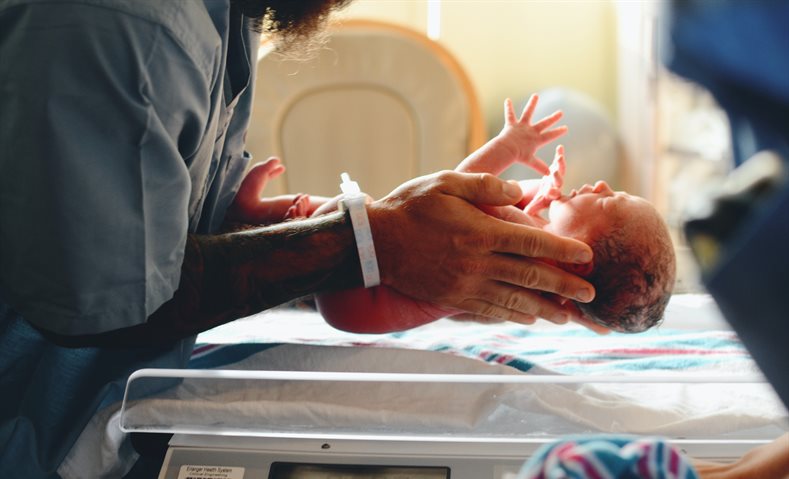 A new born baby being placed on a mat by a nurse or doctor in blue scrubs