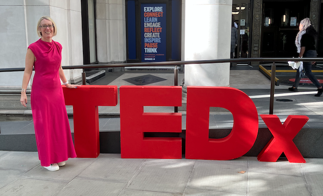 Prof Claire Smith at the TEDxNHS 2025 event outside a building next to a sign