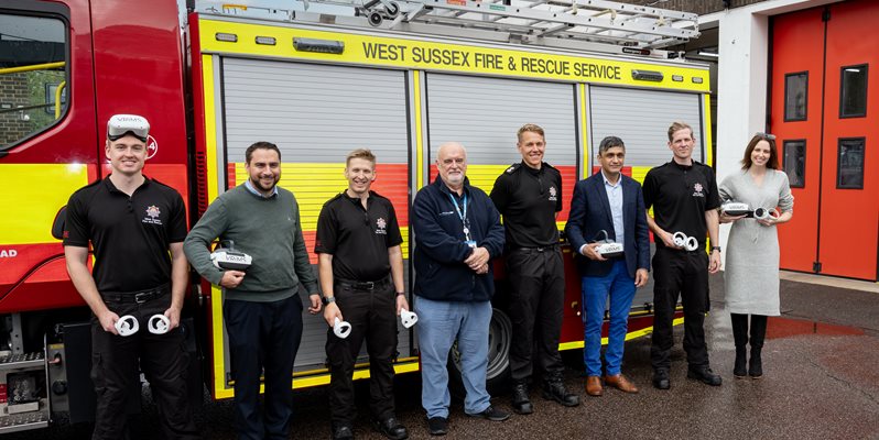 A group of people stood in front of a fire engine in a line, some wearing VR headsets