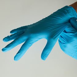 An arm of a healthcare worker putting on blue medical gloves