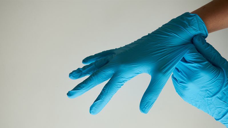 An arm of a healthcare worker putting on blue medical gloves