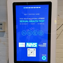 An HIV vending machine with a blue touch screen mounted to a wall