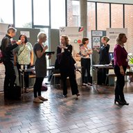 A group of people talking and looking at poster display boards in a building with windows and a tiled floor