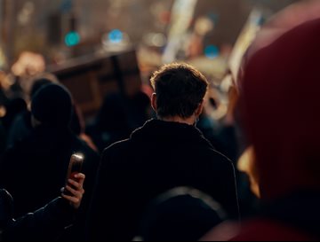 The back of a person standing in a busy crowd of people at night