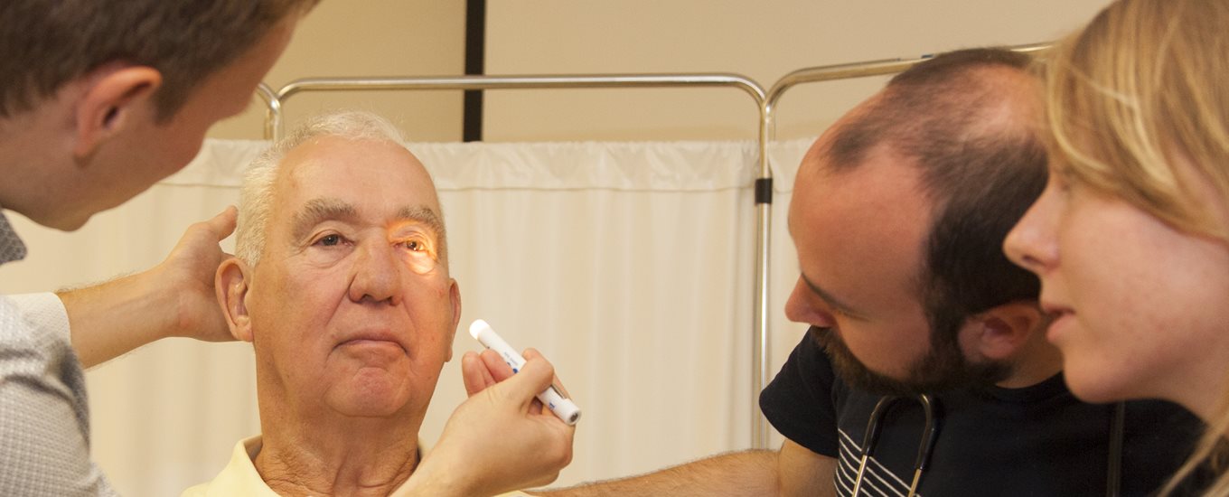 Student examining eyes of an older male patient educator with torch