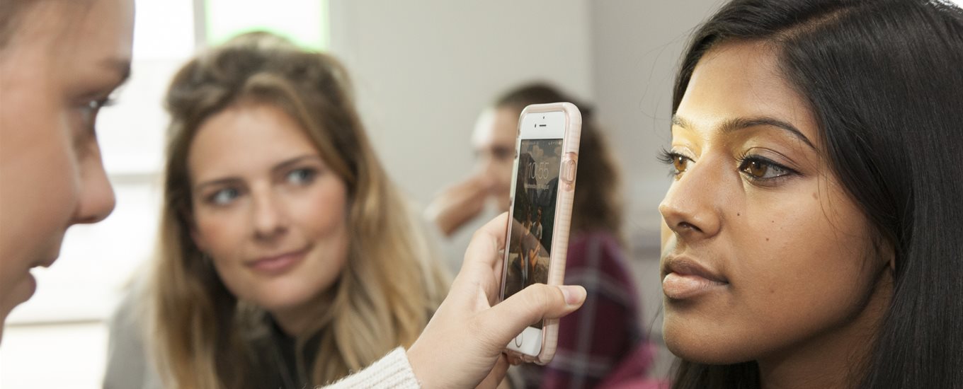 Student examining a patient's eye using a mobile phone, watched by others