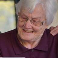 A carer with a mask on and an elderly woman smiling with an arm around her shoulder