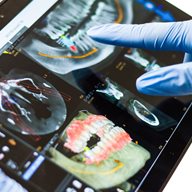 Dental implants scans on a tablet with plastic glove covered hands pointing at it