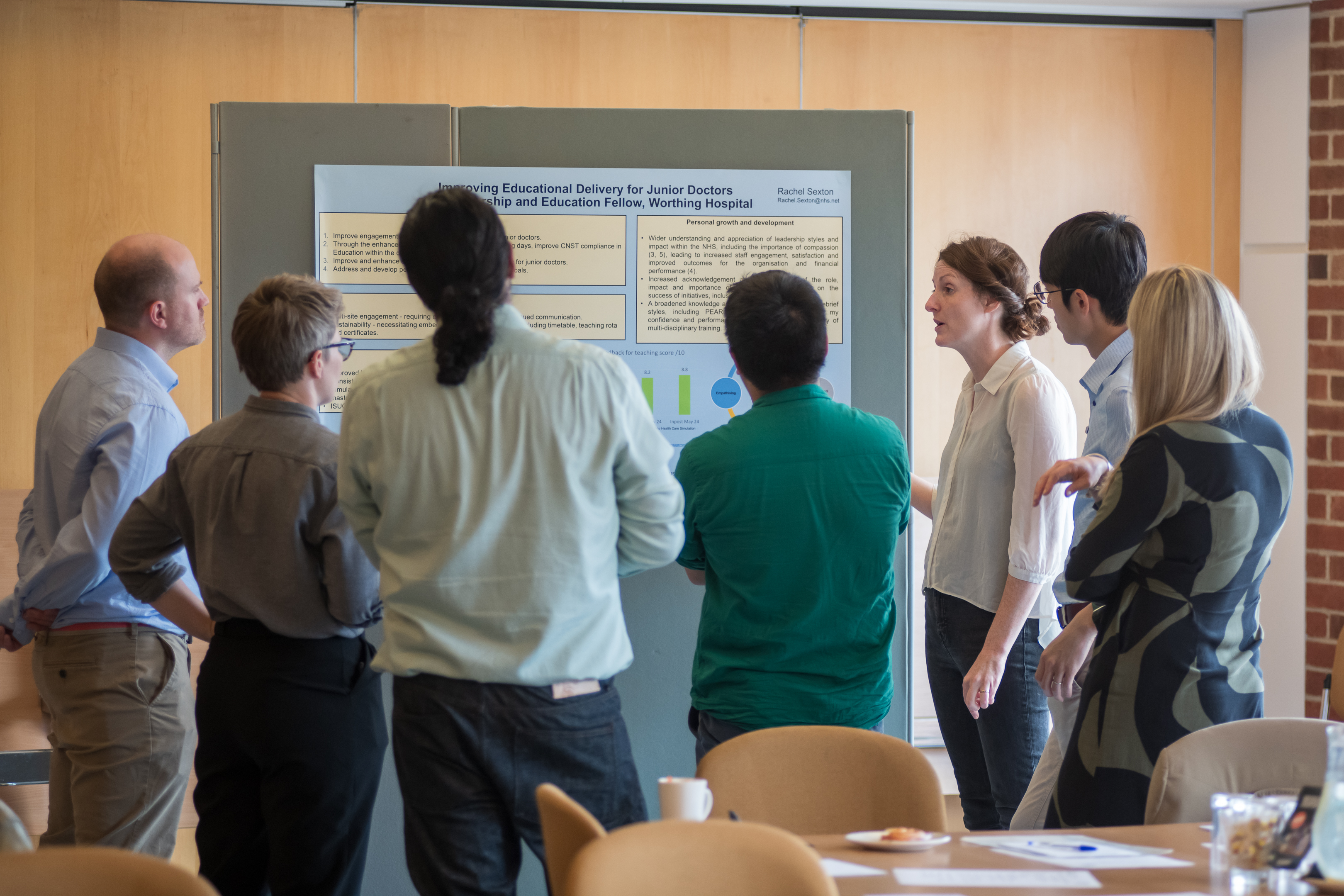 People stood around a poster presentation in a conference room