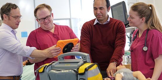 4 people in a hospital with an iPad and simulated dummy on a patient bed