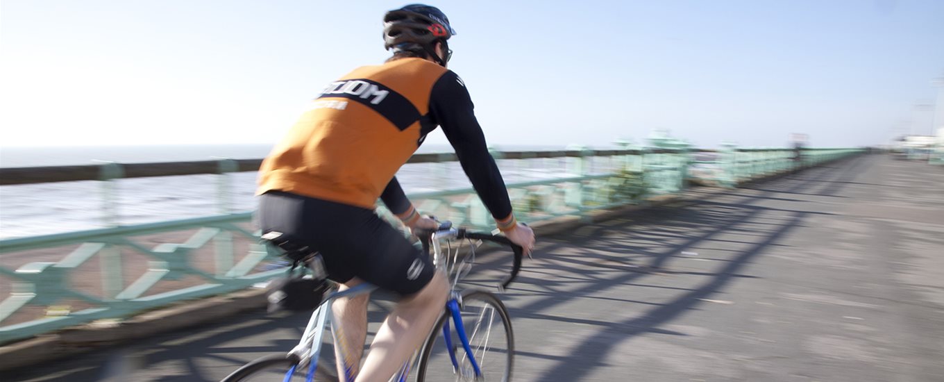 Cyclist in an orange top on a blue bike cycling along Brighton seafront