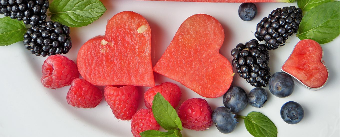 Fruit carefully arranged on a plate, with pink melon cut into hearts, raspberries, blueberries and blackberries