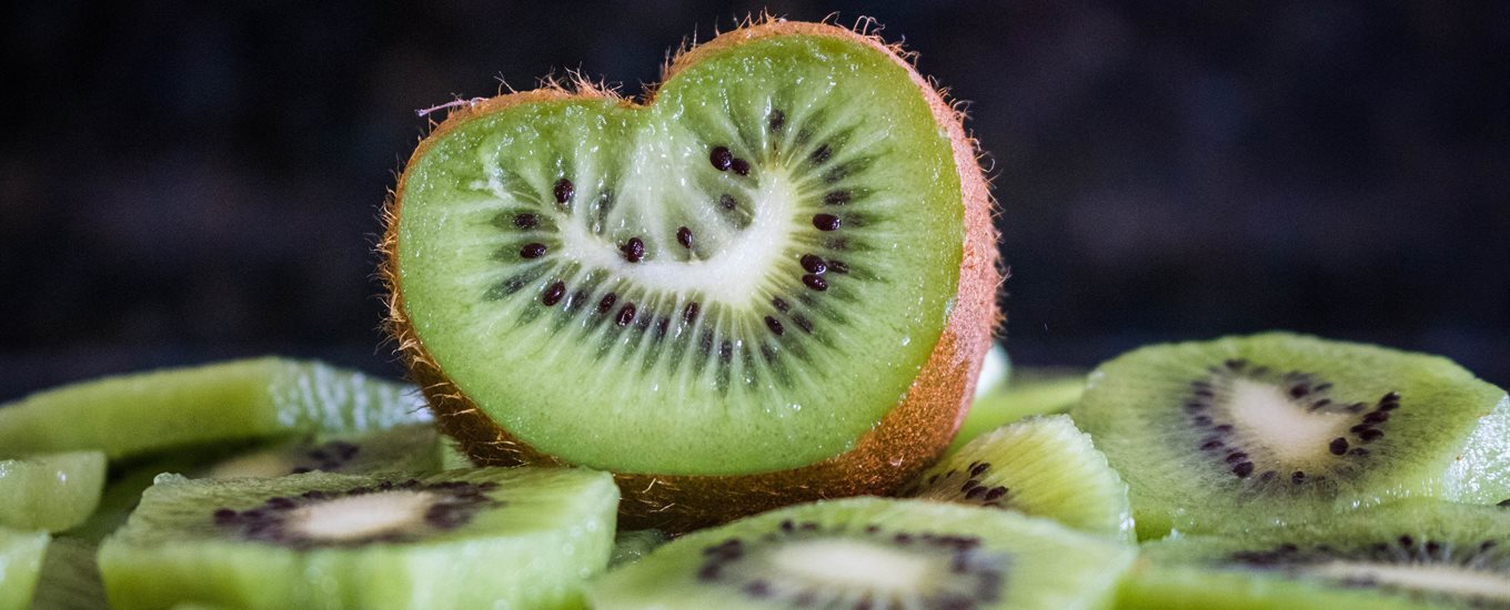 Close up of a cross section of a sliced kiwi, shaped like a heart