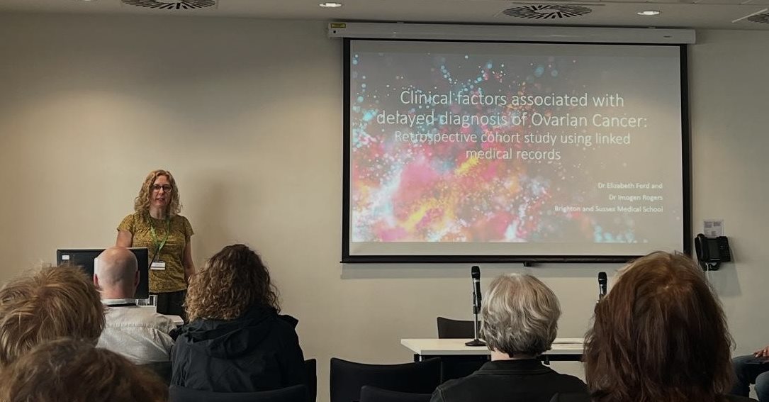 Liz Ford stood in front of a screen giving a presentation to a room of people