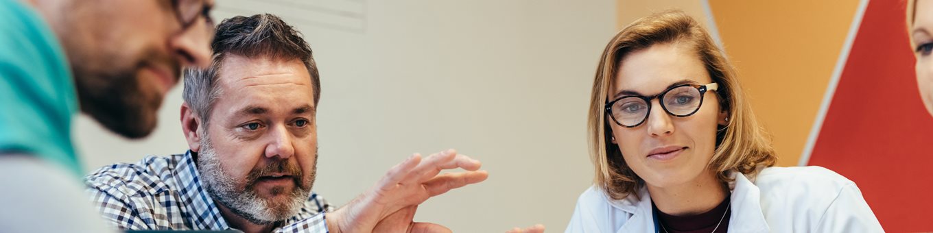 Close up of 3 people sitting in a seminar. One person is gesturing and teaching the other 2 a concept.