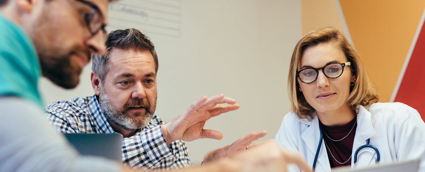 Close up of 3 people sitting in a seminar. One person is gesturing and teaching the other 2 a concept.