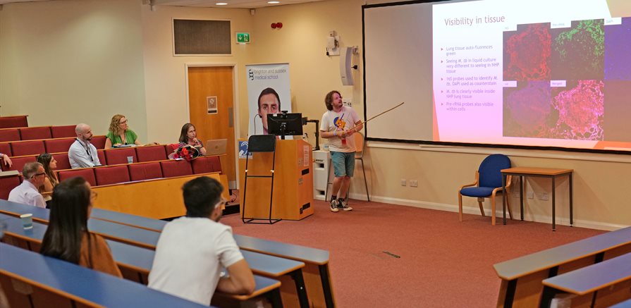 A lecture theatre with people sat looking at a presentation on the screen