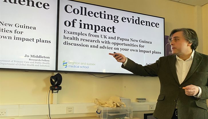 Someone stood up pointing to a screen with a presentation on it