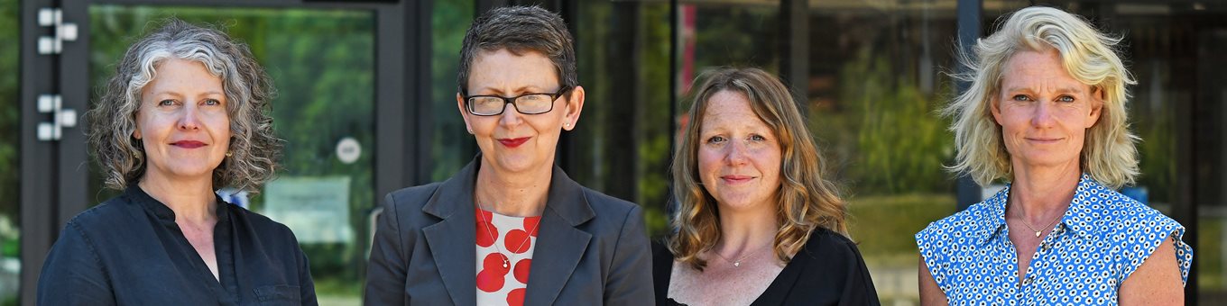 For women stood next to each other outside a building smiling.