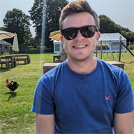 Dr Jake Bush smiles at the camera in mid close up, sitting in a garden with trees behind him